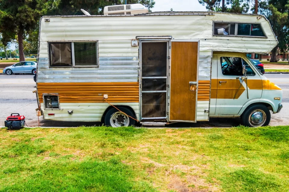 Old white motor home with brown stripe and open door parked on street in Los Angeles, California.
